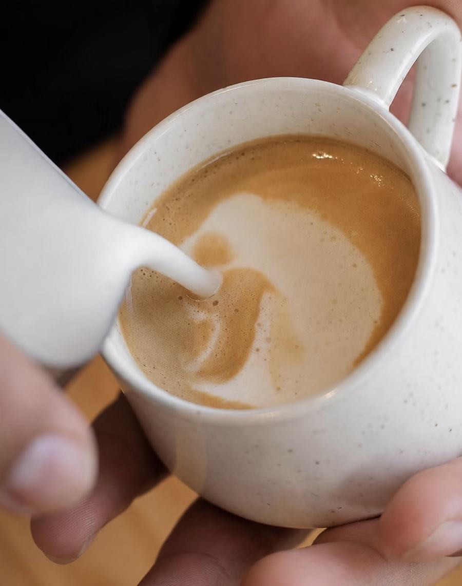 Barista sirviendo leche sobre un café en taza de cerámica moteada